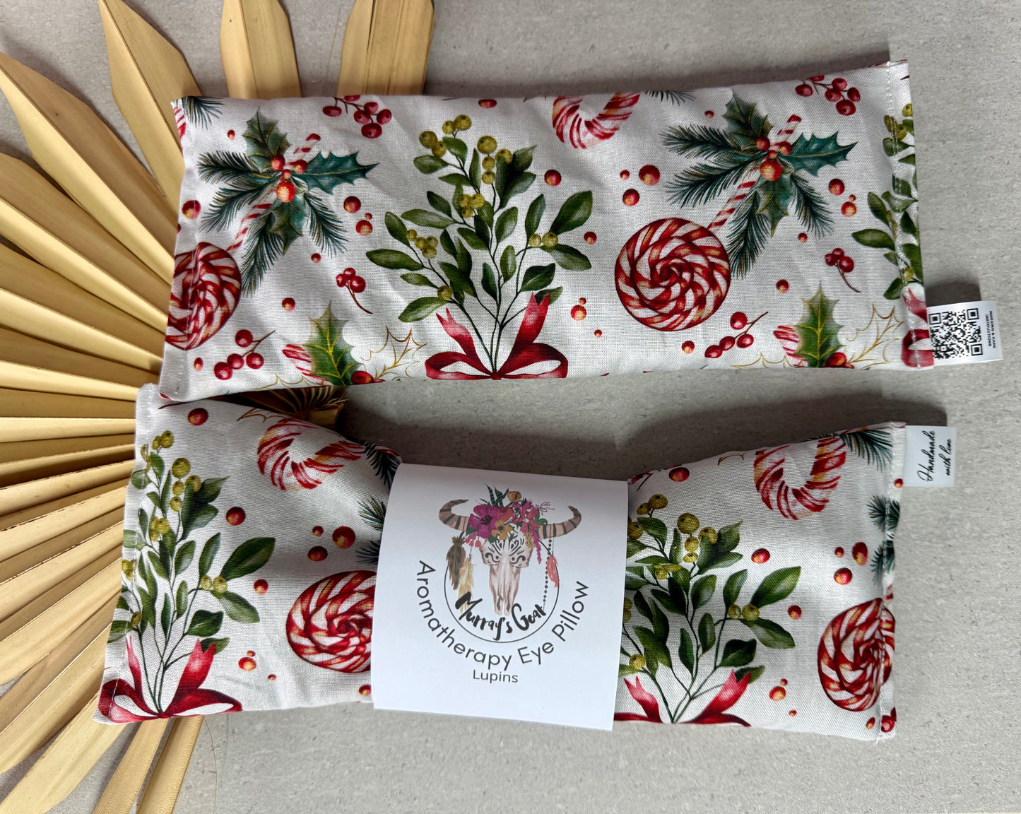 Christmas-themed eye pillow with peppermint candies and holly leaves on a gray surface.